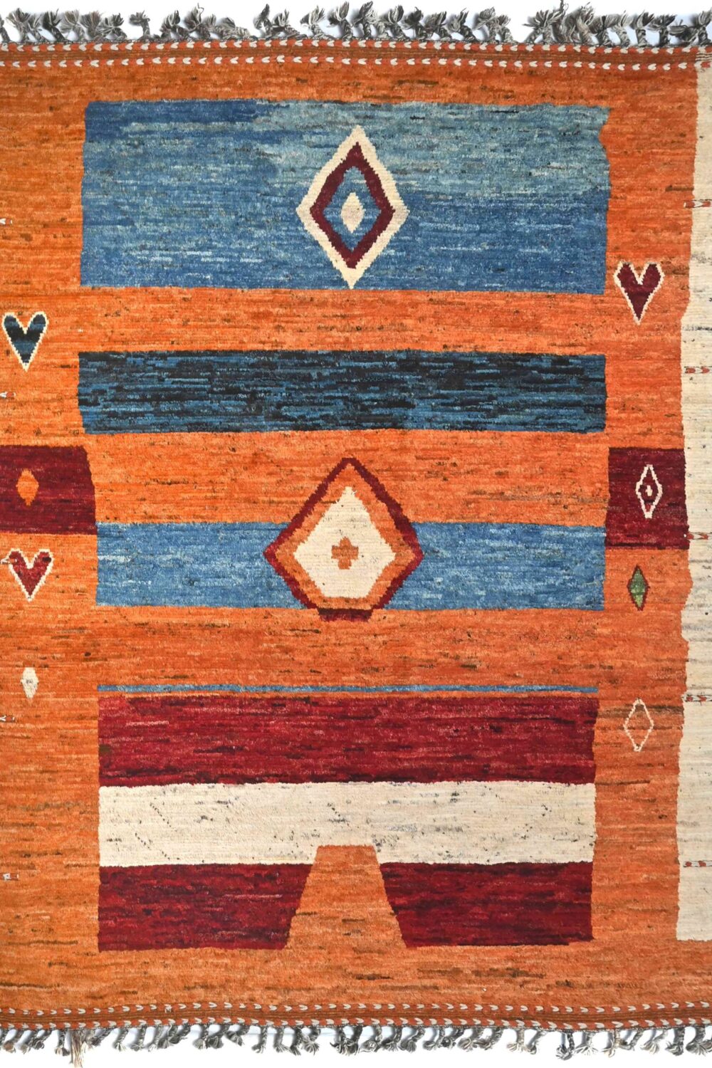 A handmade Moroccan rug 12 x 7 rug with vibrant orange, blue, and red bands, featuring diamond and heart-like motifs in white. Decorative knotted fringes complete the traditional design.