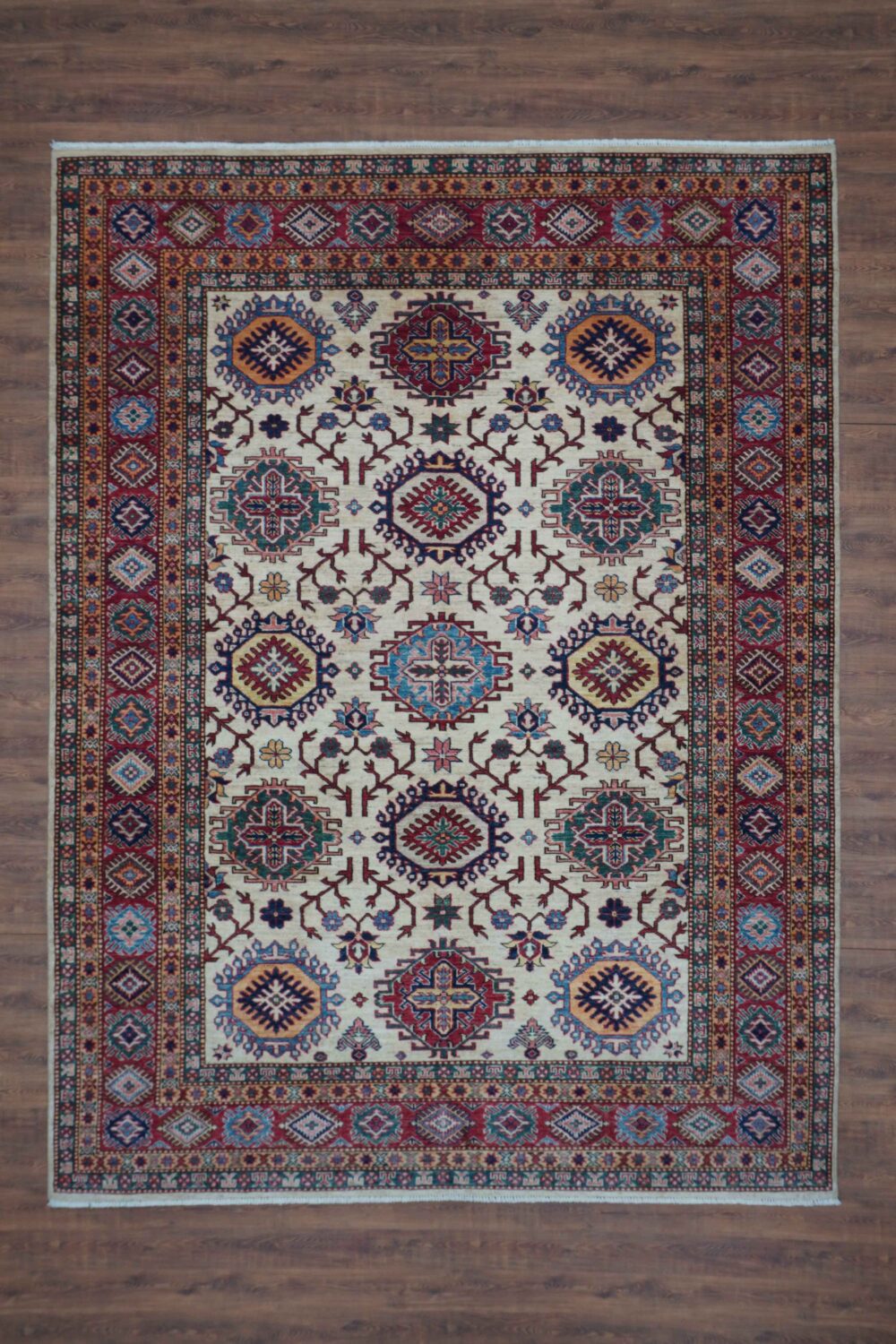 Supper kazzak Handmade rug 6 x 8 white area rug featuring intricate octagon and floral motifs in rich red, blue, and gold hues. Highlighted by a multi-layered border with geometric patterns, this rug adds timeless elegance to any room."