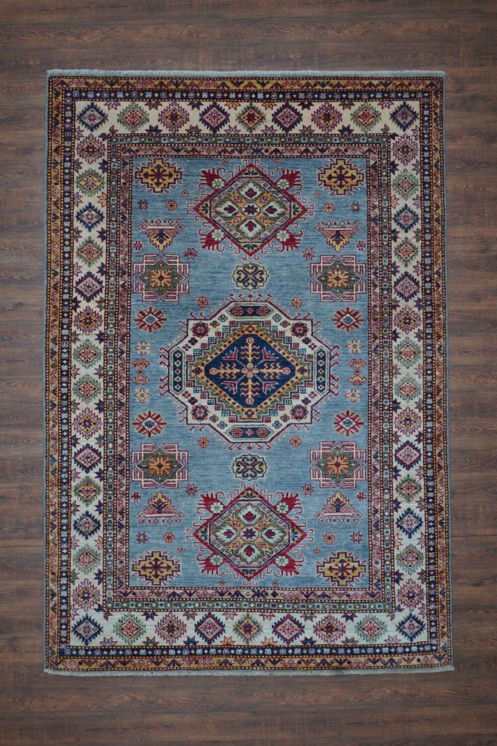 super kazzak size 5 x 7 light blue area rug with vibrant geometric and floral motifs in shades of red, yellow, and navy, bordered by a detailed ivory and multicolor traditional design, perfect for enhancing any interior space.