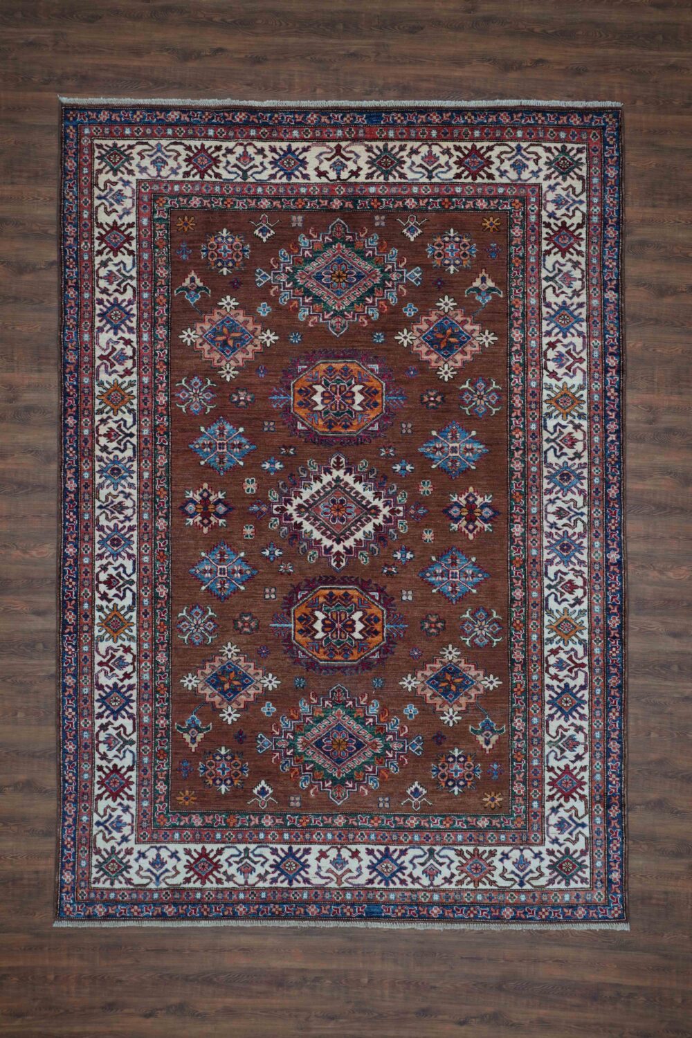 Supper kazzak 6 x 8 brown area rug showcasing geometric floral patterns in rich tones of blue, red, and ivory, bordered by intricate white accents featuring traditional motifs