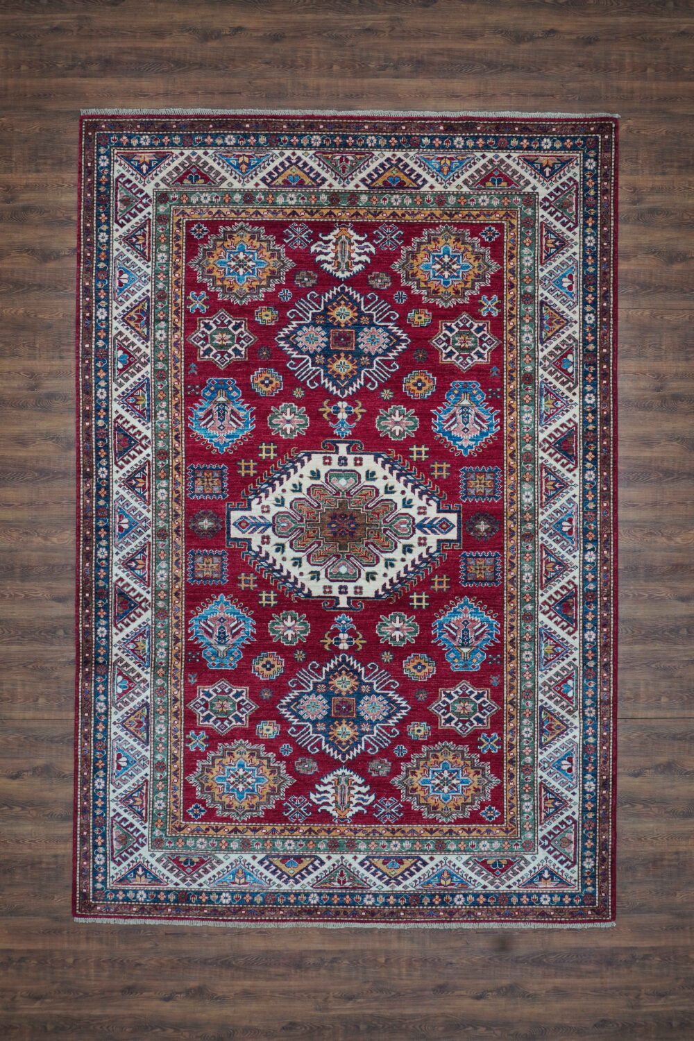 Super kazzak 6 x 8 red area rug featuring a striking central white medallion, intricate floral patterns in blue and gold accents, surrounded by a richly detailed border with geometric and traditional motifs