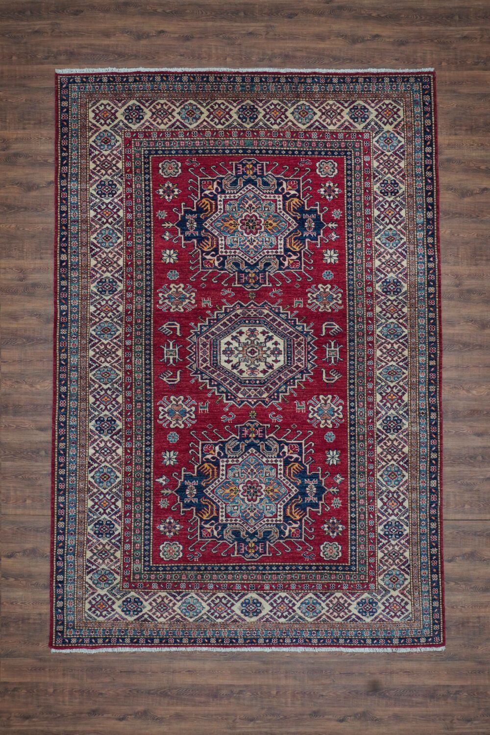 Super Kazzak 6 x 8 a bold red traditional rug featuring intricate floral patterns, blue and cream medallions, surrounded by ornate multicolored borders.