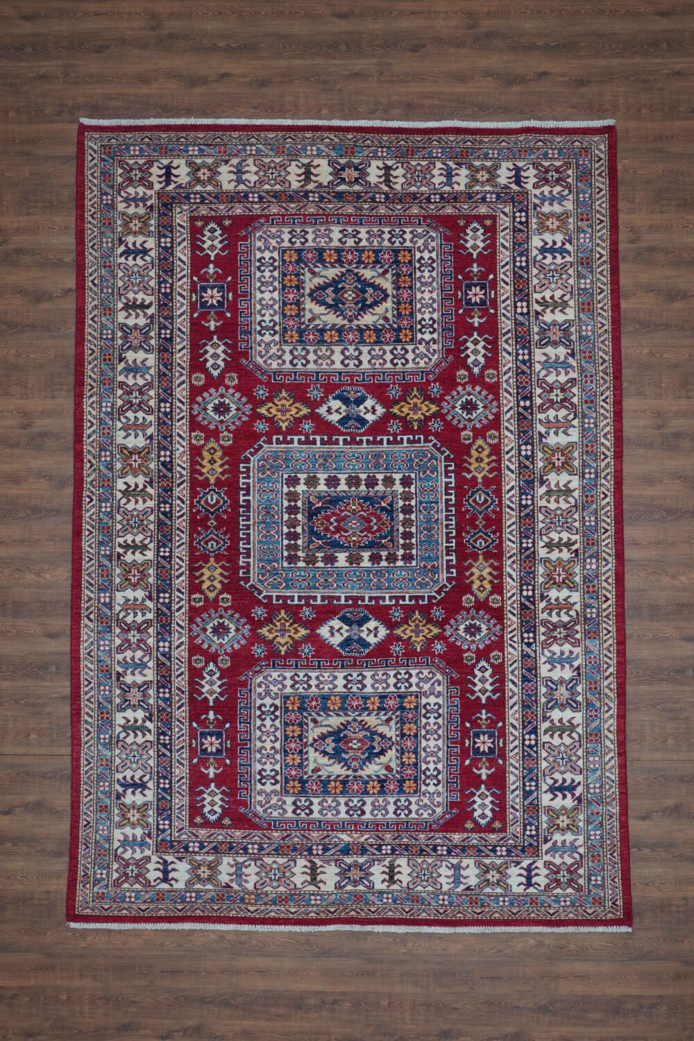 Super kazzak traditional 5x8 rug featuring a rich red background with detailed motifs in blue and white, framed by ornate floral and geometric borders, designed for use in a living room rug.