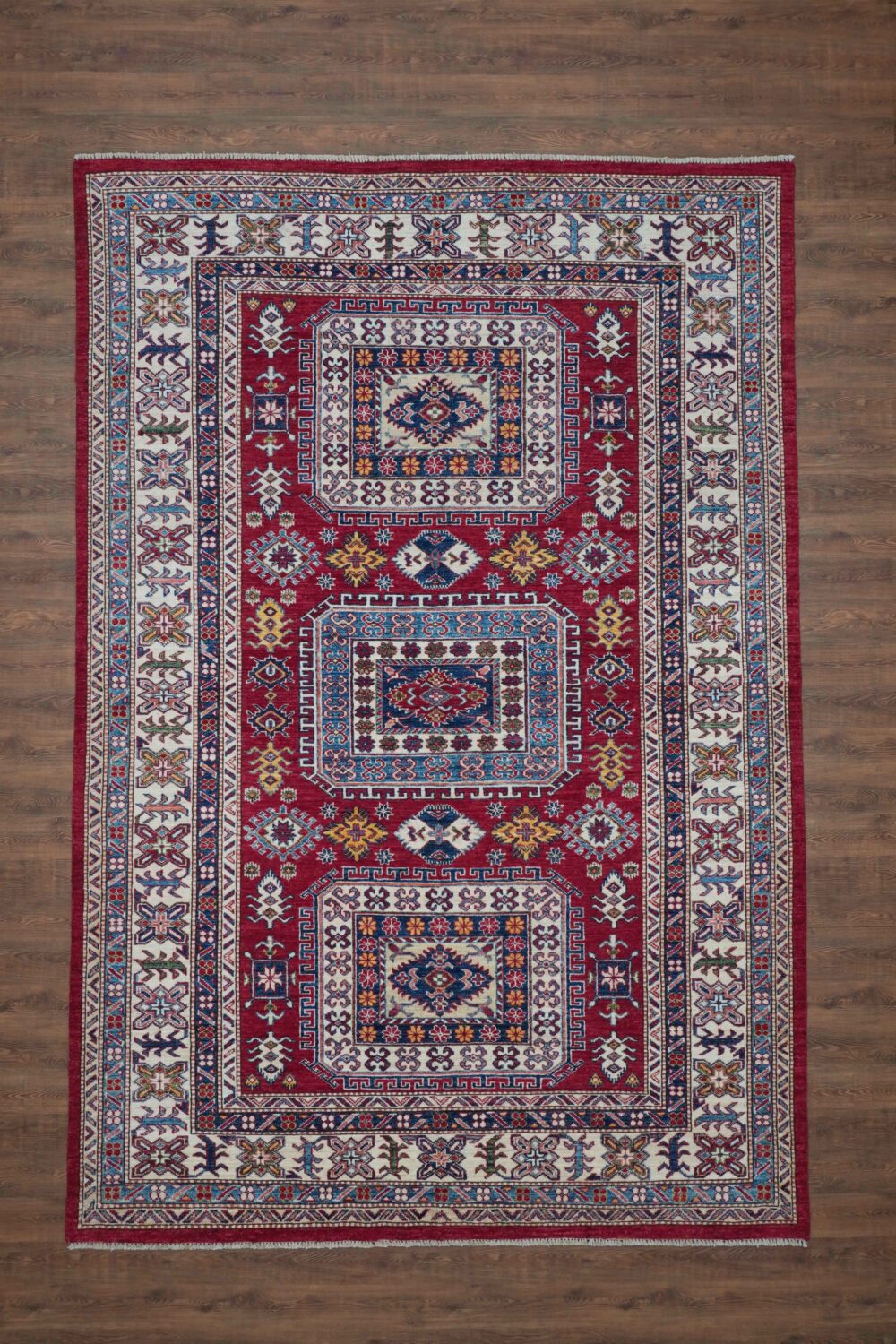 Super kazzak traditional 6 x 8 rug featuring a rich red background with detailed motifs in blue and white, framed by ornate floral and geometric borders, designed for use in a living room rug.